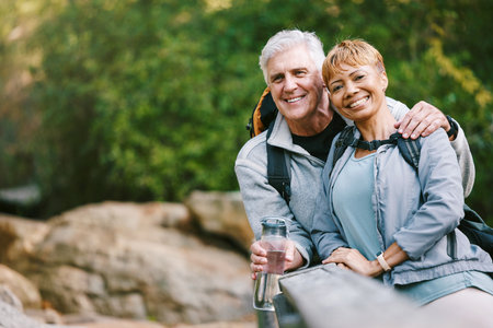 Nature, hiking and portrait of a senior couple relaxing while walking in a forest for exercise. Love, happy and elderly people with a smile sitting to rest while trekking together in the woods.の写真素材