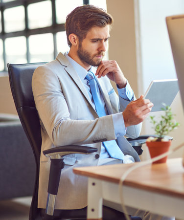 Searching for an app to suit his corporate needs. a young businessman using a digital tablet in an office.の写真素材