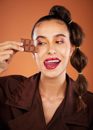 Makeup, beauty and woman with face, chocolate and lipstick, tongue out and color with cosmetics. Candy, luxury and microblading with skincare, sweets with hair care and lips against studio backgroundの写真素材
