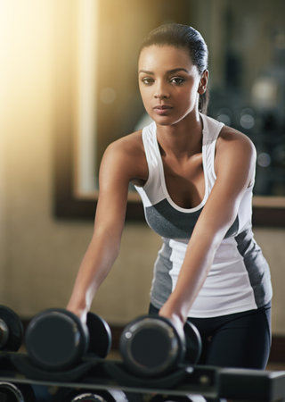 Time to work those muscles. a young woman working out with dumbbells at the gym.の写真素材