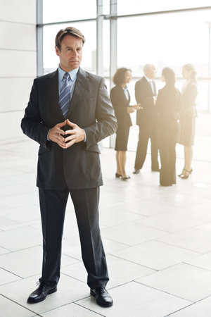 Confident and composed. Full length portrait of a businessman standing a lobby with his colleagues in the background.の写真素材