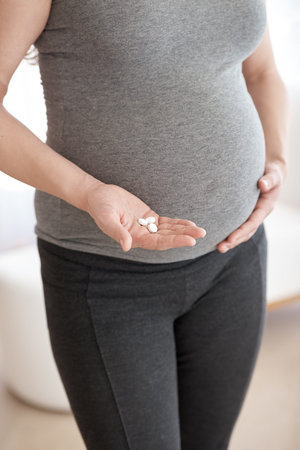 Antenatal vitamins. a pregnant woman holding tablets while standing in her home.