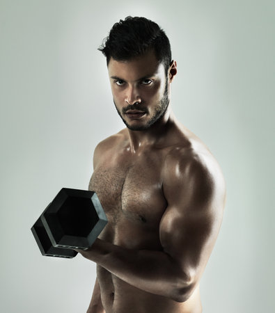 Beast mode ON. Studio shot of a young man working out with a dumbbell against a gray background.の写真素材