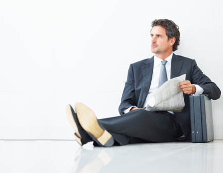Smart executive sitting against wall with newspaper and briefcase. Smart mature executive sitting against wall with newspaper and briefcase.の写真素材