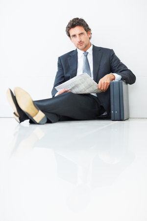 Handsome business man sitting against wall with newspaper. Portrait of handsome business man sitting against wall with newspaper and suitcase.の写真素材