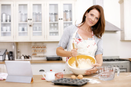 She enjoys baking. Portrait of a mature woman baking in the kitchen.