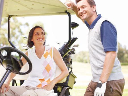 Hes winning this round of golf...Smiling woman seated in a golf cart with her husband standing alongside her.の写真素材