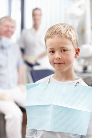 Smiling boy at dentists office. Portrait of cute young boy smiling with doctors in background.の写真素材