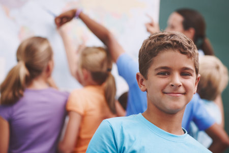 The world awaits. A cute young boy smiling at you as his classmates and teacher look at a world map...