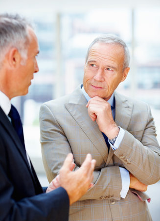Senior executive discussing proposal with partner. Business man listening to colleague with arms folded.の写真素材