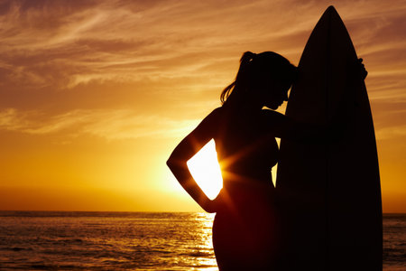 Silhouetted woman with surfboard against scenic sunset by sea. Silhouette image of woman with...