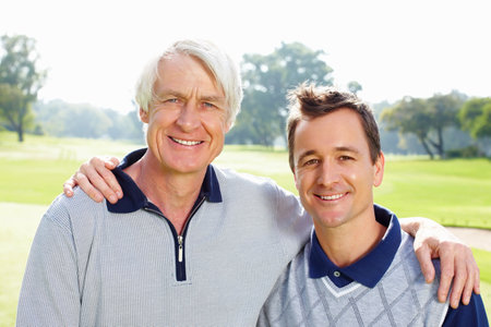 Father and son on the golf course. Closeup of father and son standing on golf course with arms around and smiling.の写真素材