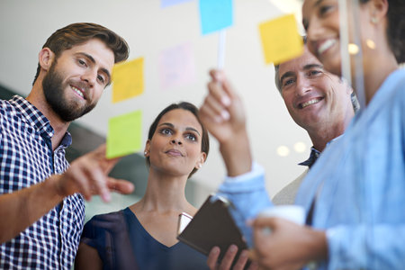 Teamwork makes the dream work. coworkers arranging sticky notes on a glass wall during a...