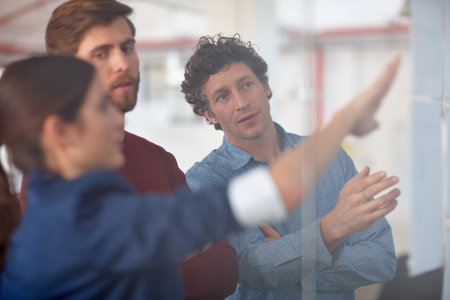 Collaborating on a creative project. A group of creative professionals working together at a glass wall with designs on it.の写真素材