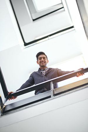 Hows it going down there. Low angle portrait of a young businessman leaning on a stairwell bannister.の写真素材