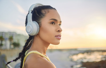 Headphones, exercise music and woman at beach thinking about training, exercising or workout. Sports, fitness and female athlete streaming radio, podcast or audio after running at sunset by ocean.の写真素材