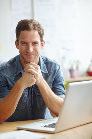 Relaxed attitude at work. A young man sitting at his desk while smiling at the camera.