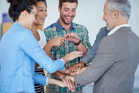 One, two, three...Go team. a group of happy coworkers standing with their hands together in huddle...