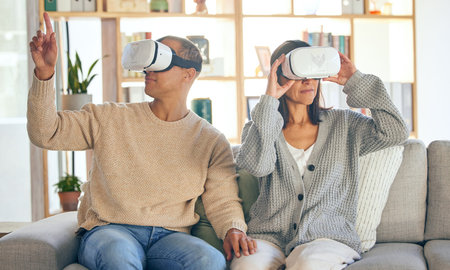 Virtual reality, 3d and a couple in the interactive metaverse while together on a sofa in the living room of a home. VR, goggles and gaming with a man and woman in their house to relax or video gameの写真素材
