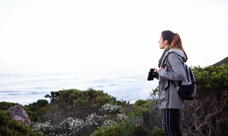 Searching the skies and scenery. a young woman using binoculars while out hiking.