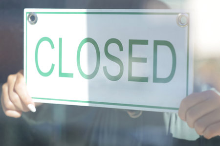 Closed, sign and window with a small business owner or entrepreneur hanging a signage notice behind closed. Management, store and retail with a woman employee in a shop to hang a poster on a doorの写真素材