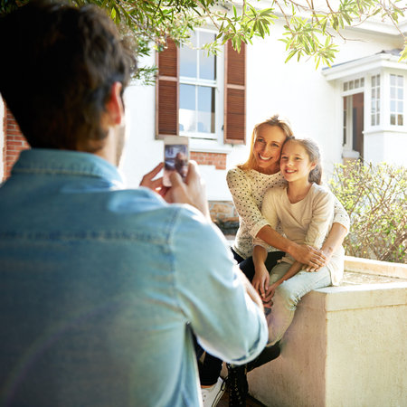 capture every moment. A man using his smartphone to take a photo of his family sitting outdoors.