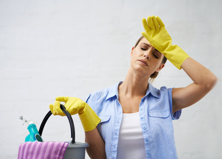 Time to get a housekeeper. a woman holding cleaning supplies and wiping her forehead.の写真素材