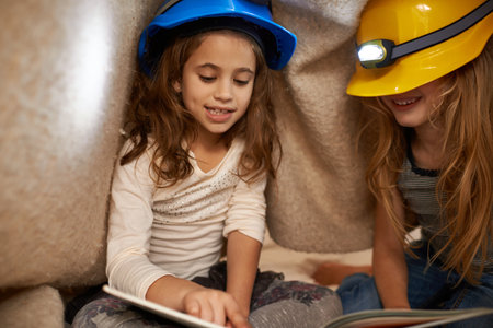 Reading their favorite stories. two little girls reading underneath a blanket using headlamps.の写真素材