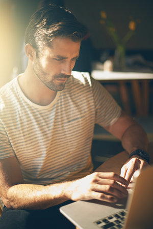 Updating the content on his website. a young man working on his laptop in a coffee shop.の写真素材