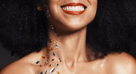 Woman face, fashion jewelry or body art rhinestones on black background studio in festival diamonds sparkle or creative party crystals. Zoom, happy smile or beauty model skin and makeup cosmetic gemsの写真素材