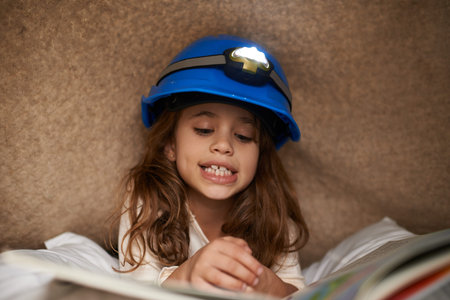 Getting lost in the story. a cute little girl reading underneath a blanket using a headlamp.