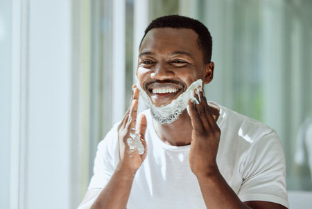 Shaving, cream and black man grooming face for clean look, hygiene care and beauty morning routine in the bathroom. Skincare, happy and African person ready to shave beard and facial hair with foamの写真素材