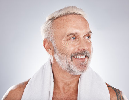Senior man, beauty and skincare while grooming, happy and clean after a shower with a towel on a gray background. Face of a old male model with a smile for cosmetics, dermatology and healthy skinの写真素材