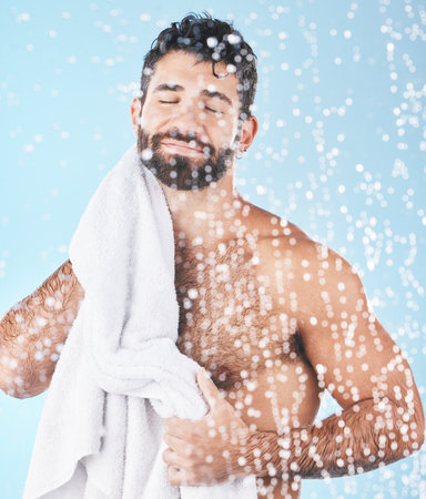 Clean, man with towel and beauty, body hygiene with bokeh overlay and grooming against blue background. Skincare with shower and smile, clean cosmetic care and cotton fabric, facial and wellnessの写真素材