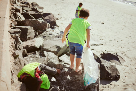 Environment, cleaning and children with dirt on beach for clean up, pollution and eco friendly volunteer. Sustainability, recycle and kids reduce waste, pick up trash and plastic bag on beach sandの写真素材