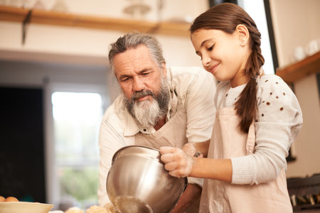 Mixing things up. a girl and her grandfather baking together.の写真素材