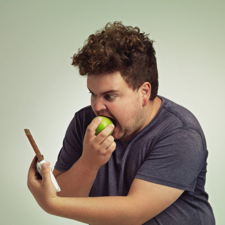 Dodge temptation - stick to your diet. an overweight man taking a bite of an apple while looking at...