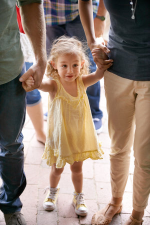The world is so cool from down here. An adorable little girl holding her parents hands while walking through the street.の写真素材