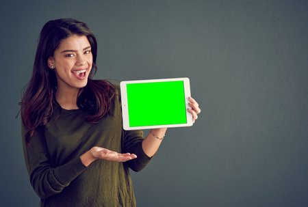 The most convenient device on the market. Studio shot of an cheerful young woman holding a digital tablet while standing against a dark background.の写真素材