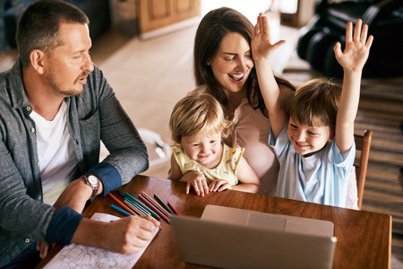 Educational games make learning so much fun. a little boy raising his arms enthusiastically while using a laptop with his family at home.の写真素材