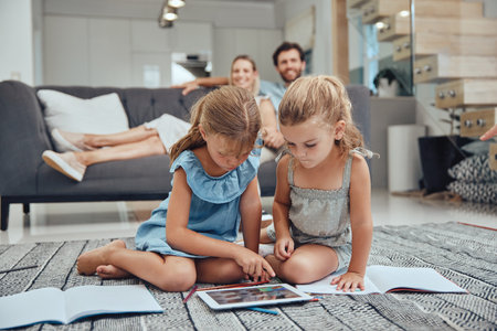Living room, parents relaxing and children doing elearning on tablet in books on the floor in their home. Mother, father and girl kids sitting in lounge together for homeschool learning and studying.の写真素材