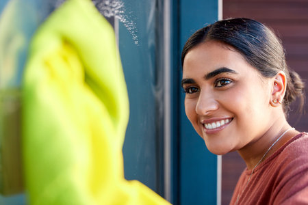 Woman, cleaning and window washing with a smile to clean windows dirt with water, soap and fabric. Happy Indian person cleaner or maid doing spring cleaning with happiness for housekeeping helpingの写真素材