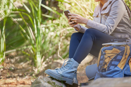 Communication, phone and legs of woman in nature to relax, search gps location and trekking during travel in Nepal. 5g connection, chat and girl on a mobile app for internet while hiking in a forestの写真素材