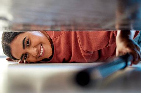 Woman cleaning under a bed in bedroom with vacuum for the floor to clean dust, dirt or bacteria. Happy, smile and portrait of housewife or maid disinfecting the ground of house while spring cleaning.の写真素材