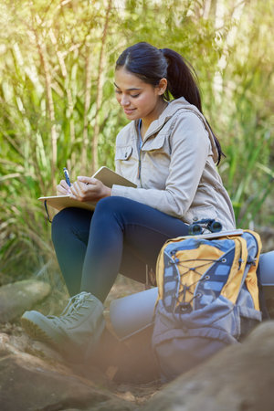 Hiking, travel and woman writing in book sitting outdoors in nature. Freedom, hiker and happy female from India with personal diary, notebook or journal to write ideas, thoughts or journey experienceの写真素材