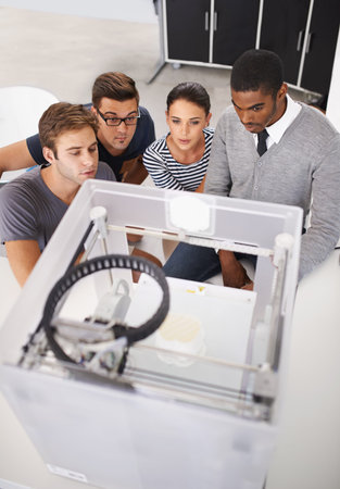 Fascinated by modern technology. a group of designers looking at a 3D printer.