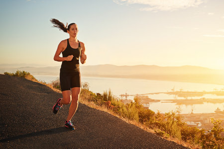 Motivated to achieve her fitness goals. a young woman running along a scenic route.の写真素材