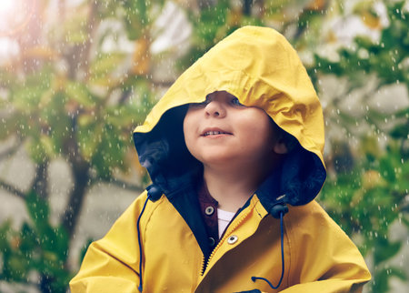 Check out my cool rain jacket. an adorable little boy playing outside in the rain.の写真素材
