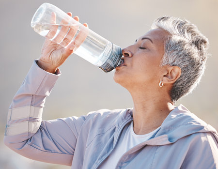 Fitness, wellness and senior runner drinking water for hydration on outdoor run, marathon training or cardio workout. Sports exercise, bottle and profile of thirsty woman running in Miami Florida USAの写真素材