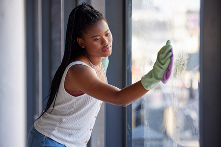 Housework, hygiene and black woman cleaning the window with cloth while doing housekeeping. Cleaning service, routine and African female cleaner, maid or housewife washing glass door for dust or dirtの写真素材